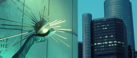 A modern sculpture with a spherical element and radiating lines, set against a backdrop of tall buildings with reflective glass facades.
