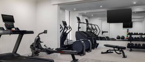 Et moderne fitnesscenter med løbebånd, crosstrainere og en bænk.