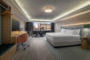 Una habitación de hotel moderna con una cama grande, un escritorio con silla, un televisor y una bicicleta estática.