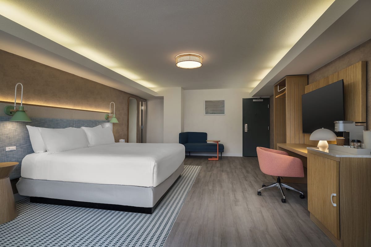 A modern hotel room with a large bed, a desk with a chair, and a television.