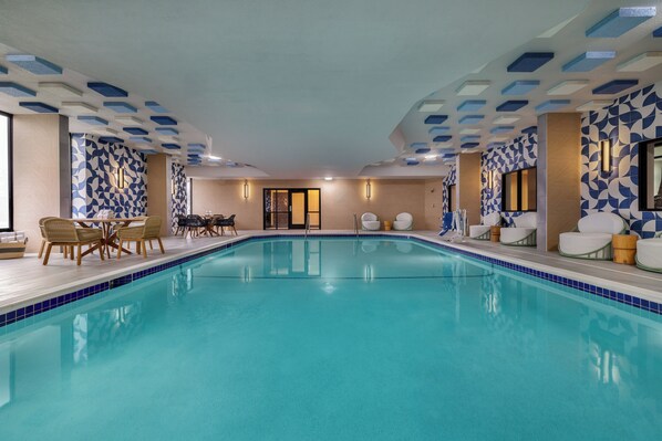 A large indoor swimming pool with tiled walls and ceiling, surrounded by lounge chairs and tables.