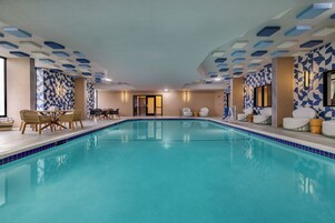 Una amplia piscina cubierta con paredes y techo de azulejos, rodeada de sillones y mesas.