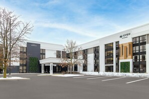 A modern hotel building with a covered entrance, large windows, and a snow-covered parking lot.