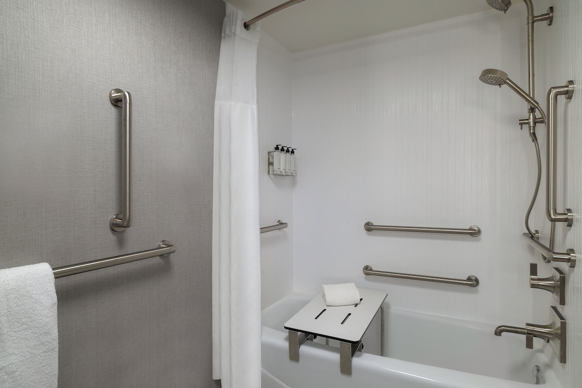 A bathroom with a bathtub, grab bars, a towel rack, and a showerhead.