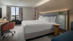 A hotel room with a large bed, a desk with a chair, a small side table, and a lamp. - EVEN Hotel Detroit North - Troy (Troy)
