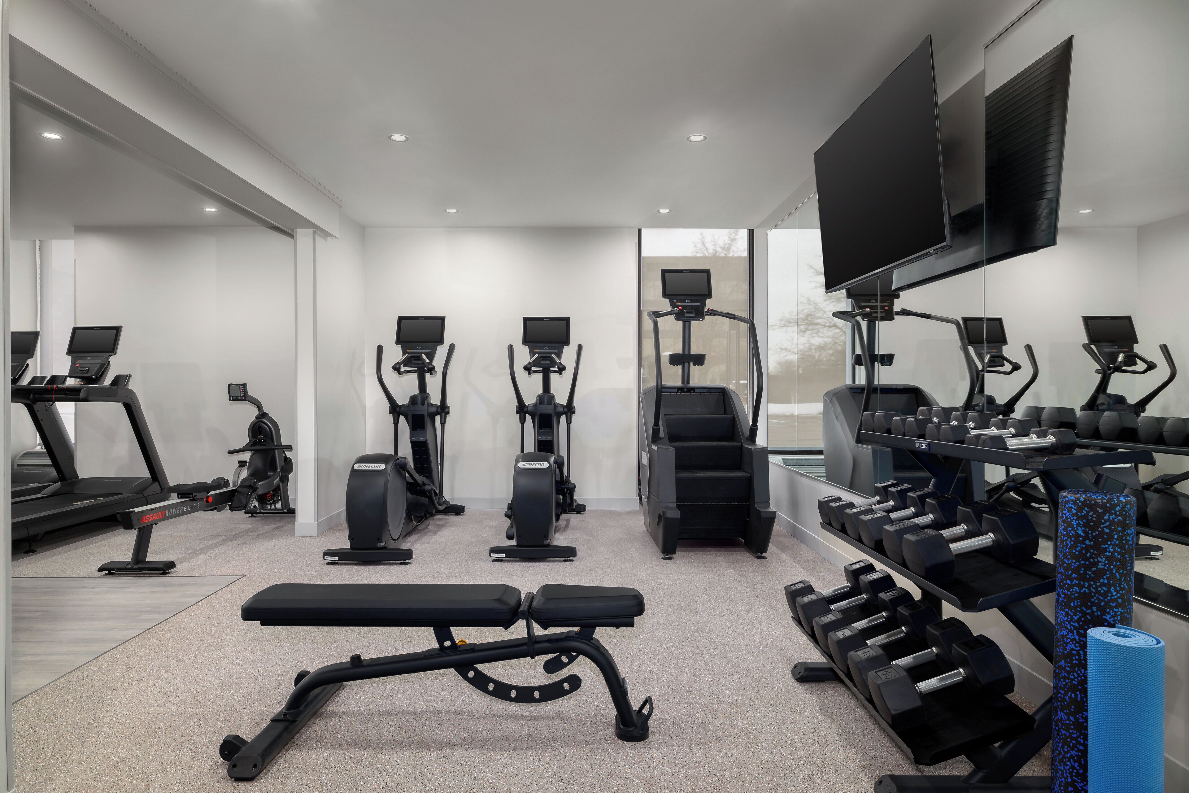 A modern gym with treadmills, elliptical machines, a bench, and weight racks.