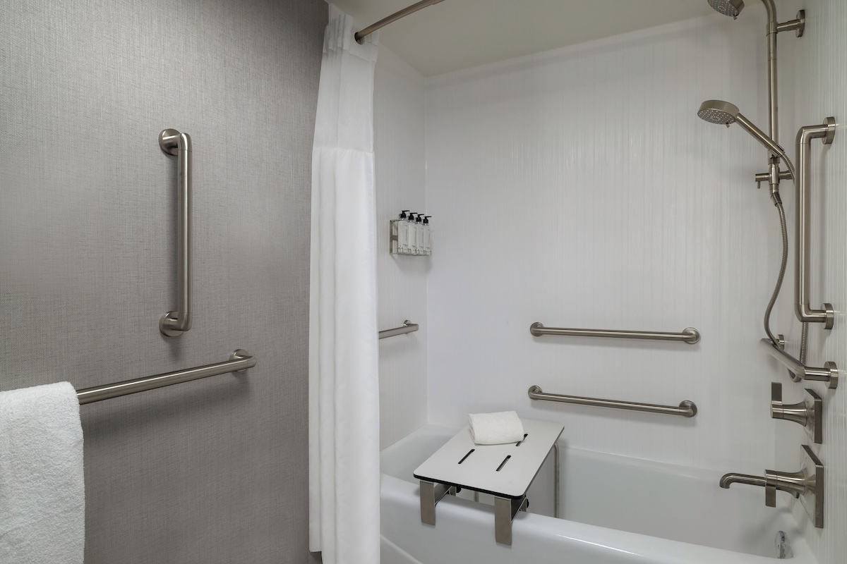 Een badkamer met een bad, handgrepen, een handdoekhouder en een douchekop.