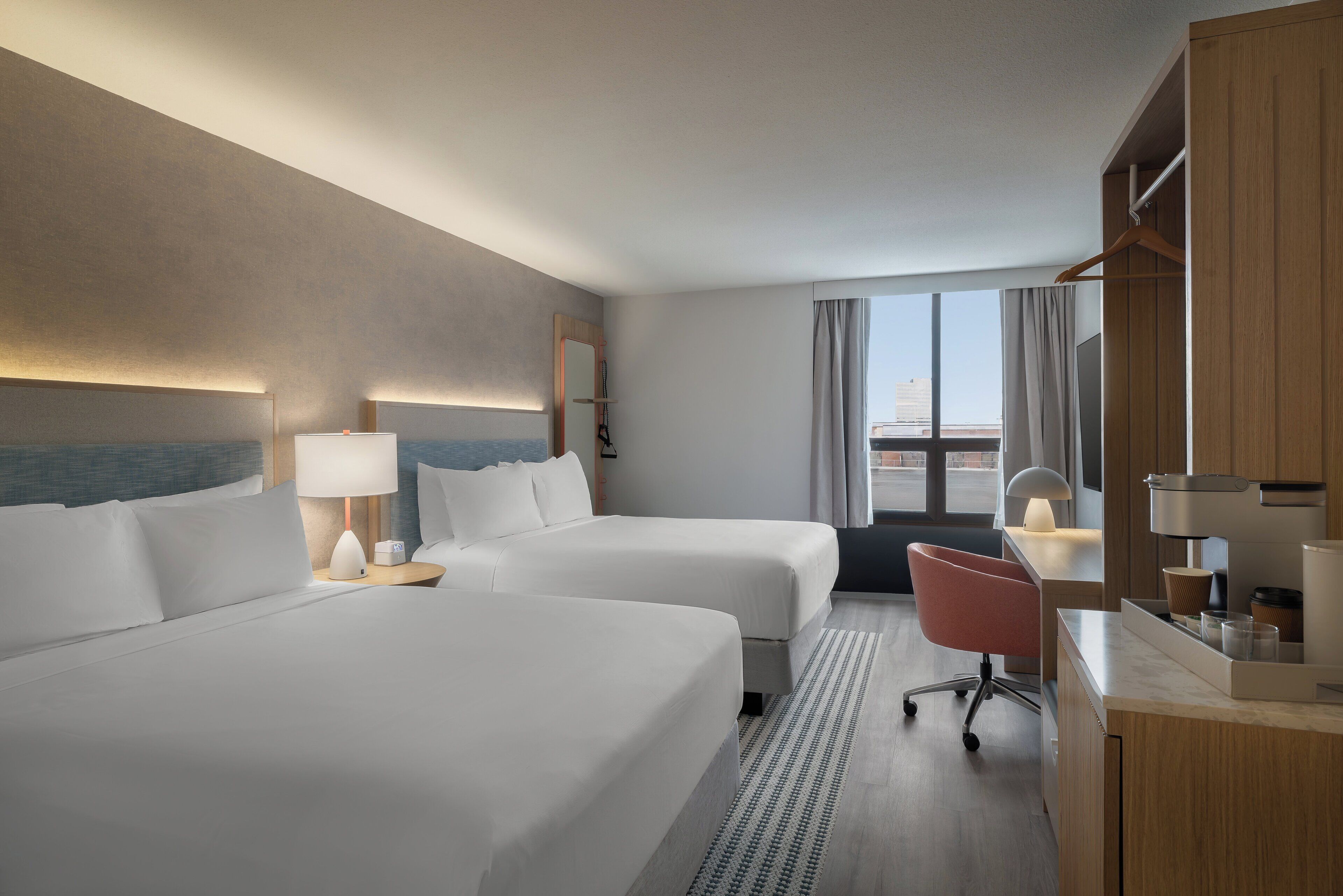 A hotel room with two beds, a desk, a chair, and a large window with curtains.