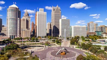 A cityscape with modern skyscrapers, a central plaza with a circular monument, and a clear blue sky.