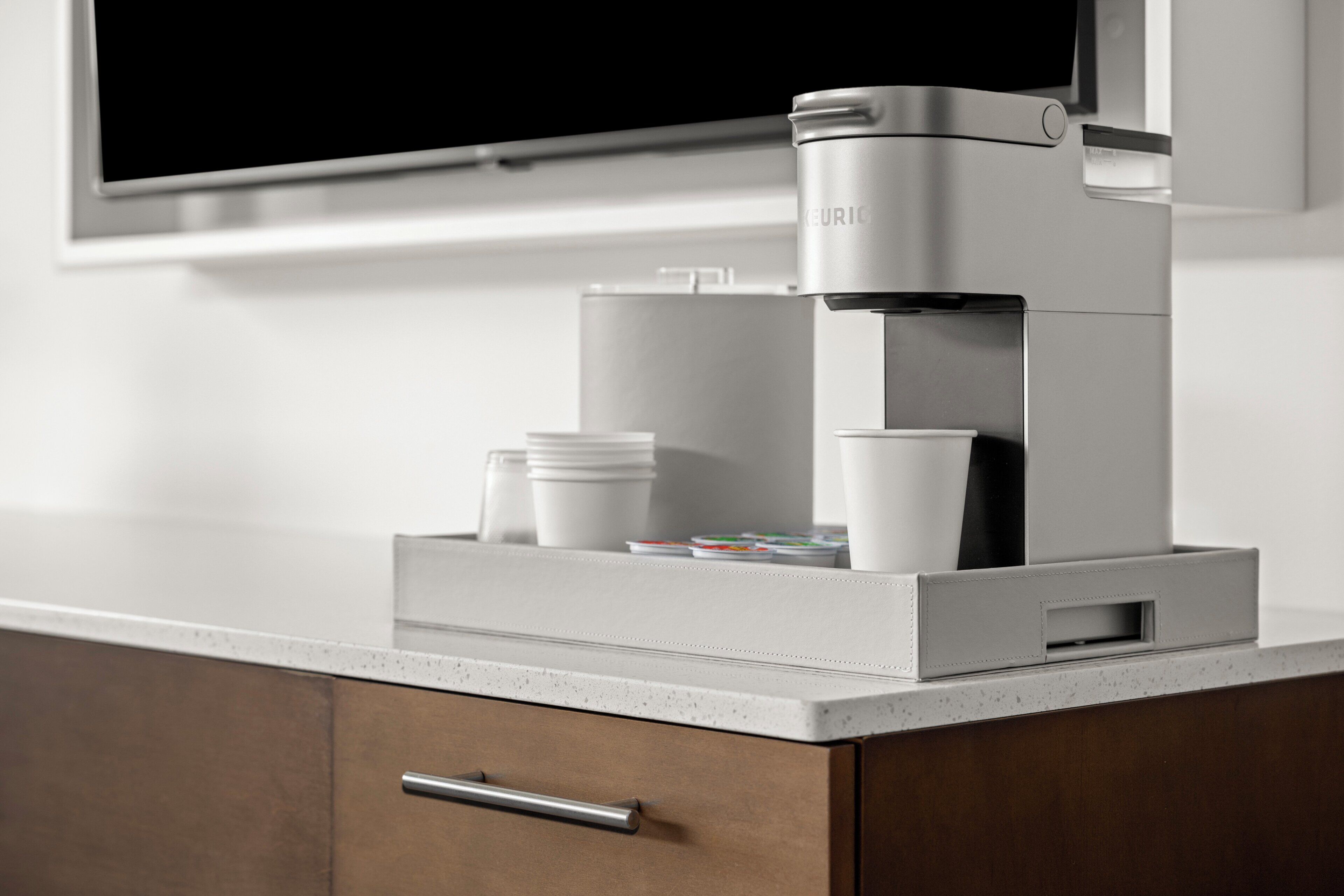 A modern coffee machine on a countertop with a television above it.