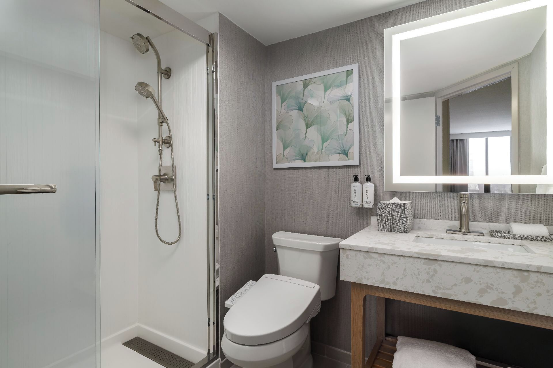 A modern bathroom with a glass shower enclosure, a toilet, a sink with a marble countertop, and a large mirror.