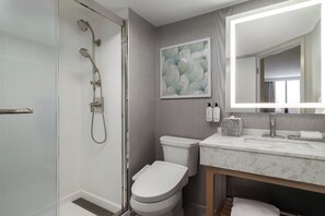 A modern bathroom with a glass shower enclosure, a toilet, a sink with a marble countertop, and a large mirror.