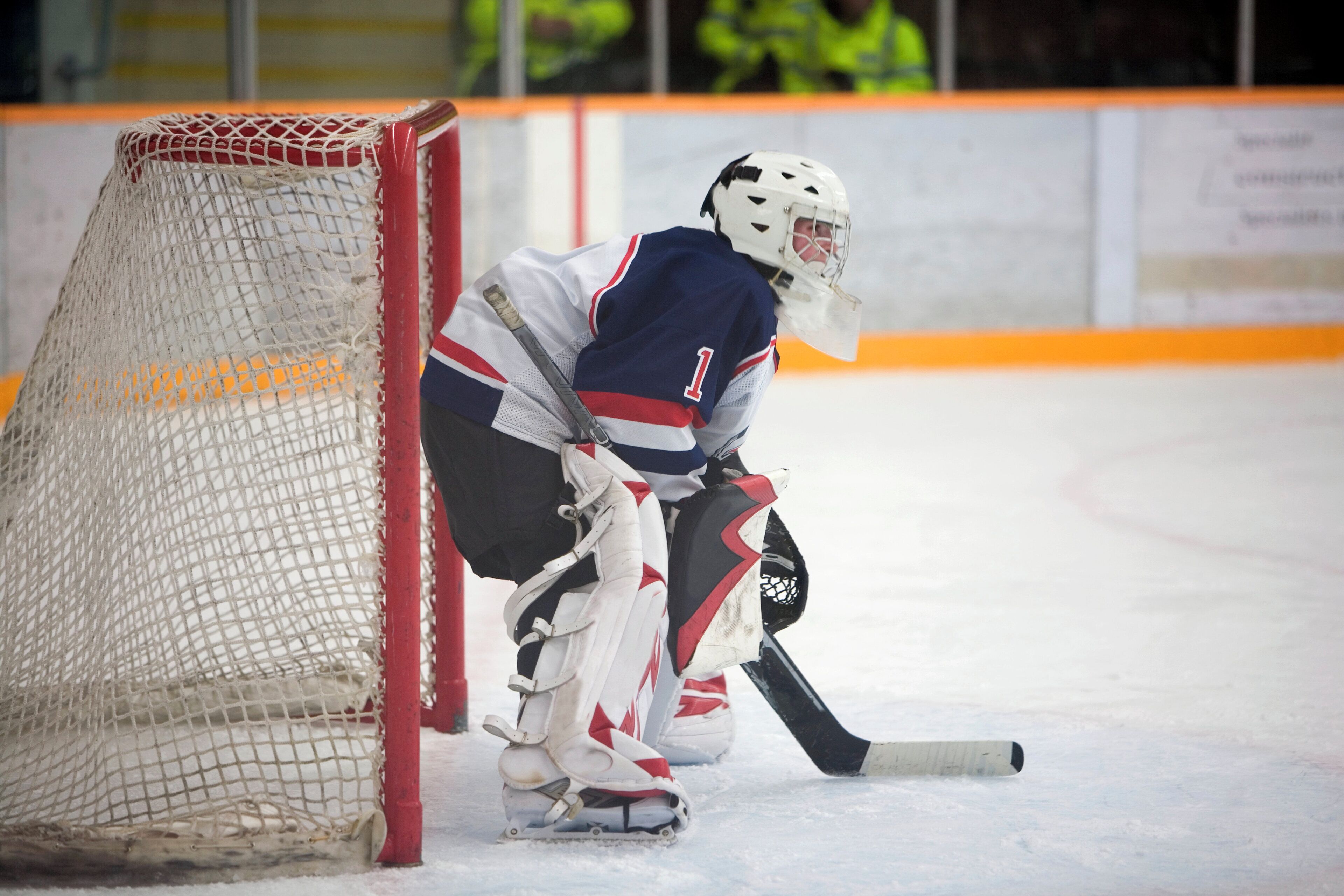 A hockey goalie in a white and blue uniform crouching near the goal net.