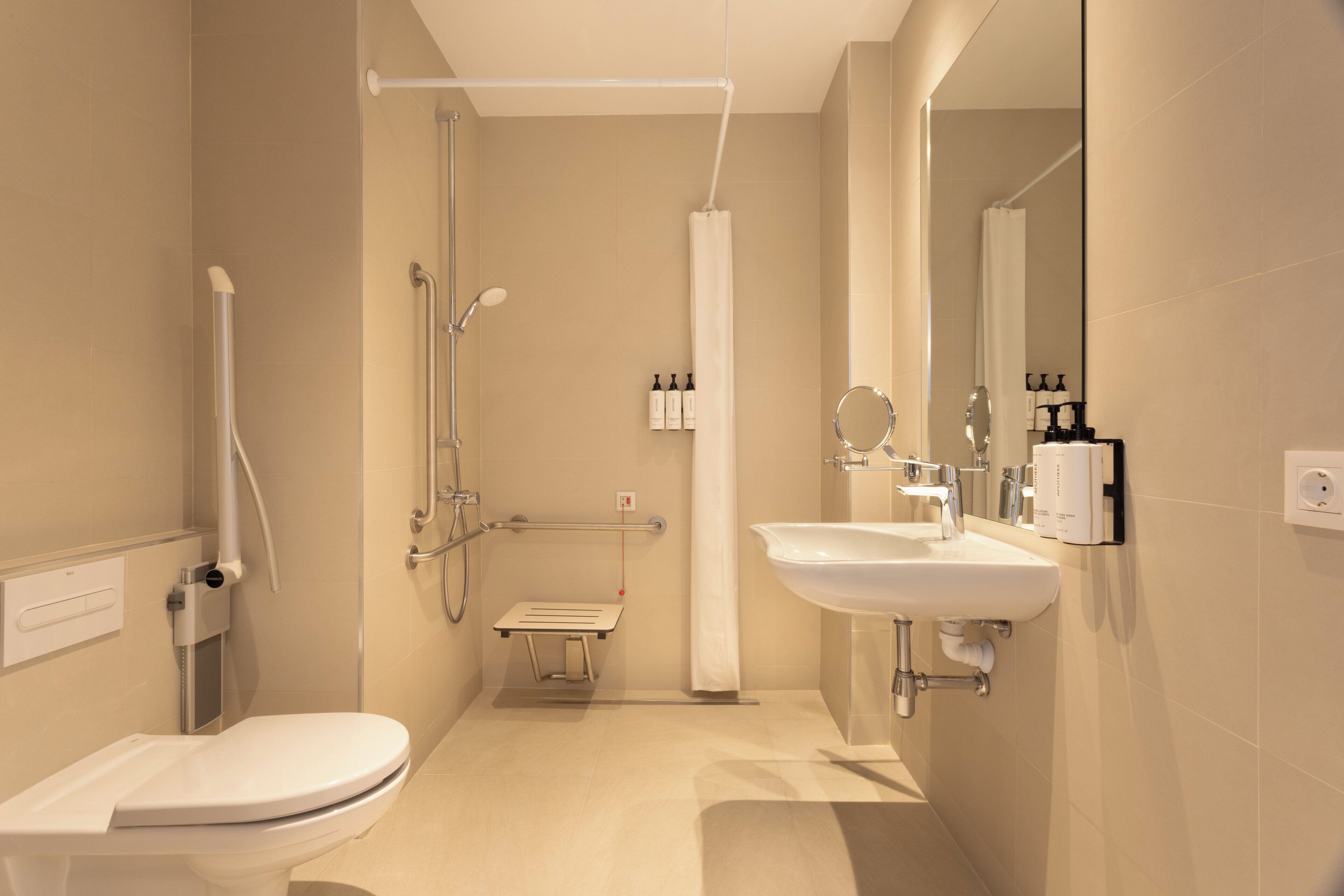 Et moderne badeværelse med toilet, håndvask, bruser og gelænder.