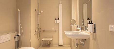 Et moderne badeværelse med toilet, håndvask, bruser og gelænder.