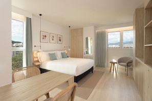 A modern hotel room with a large bed, a desk, a chair, and a view of the city. - Staybridge Suites & Apartments Malaga by IHG (Málaga)