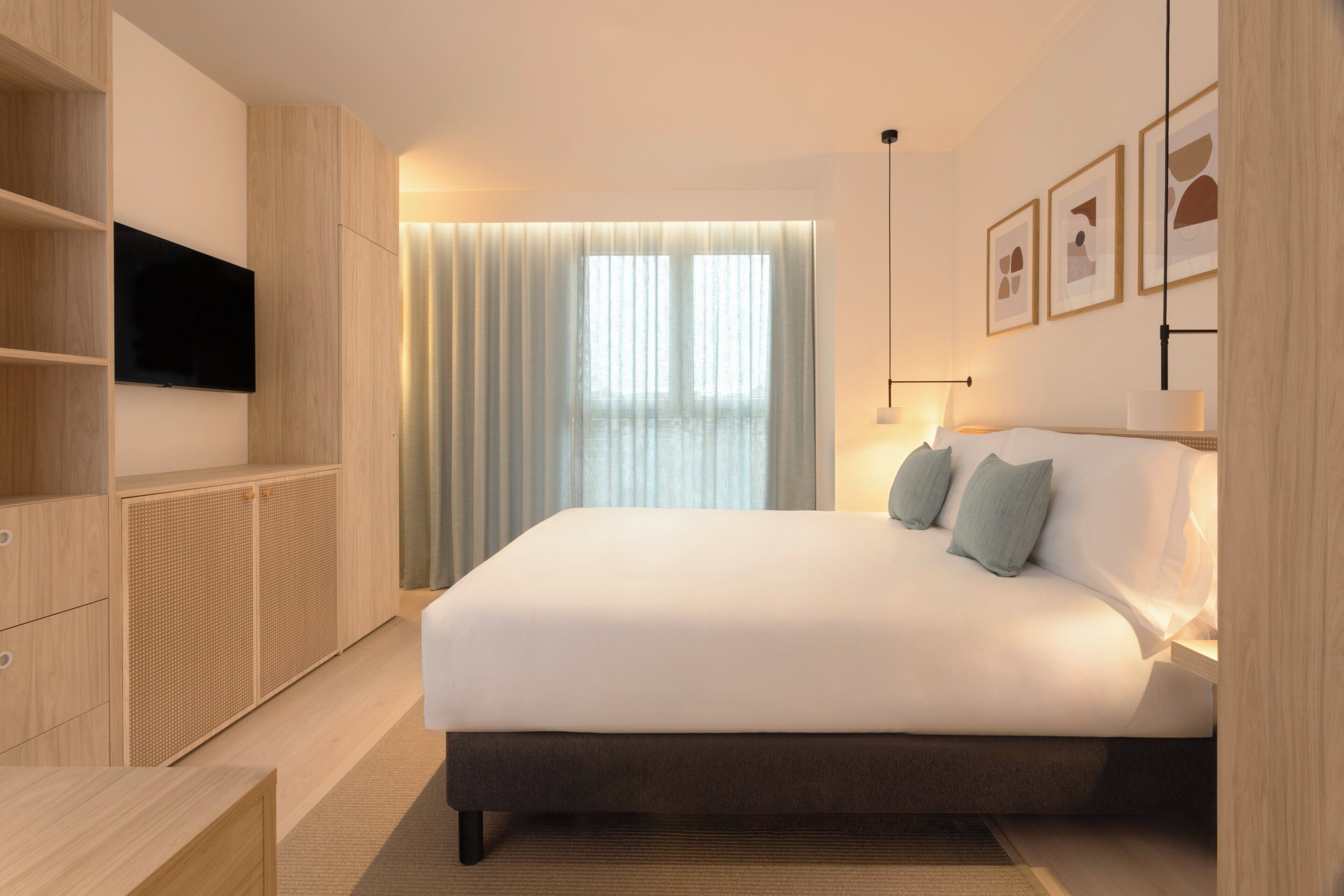 Quarto moderno com uma cama grande, televisão na parede e janela com cortinas.