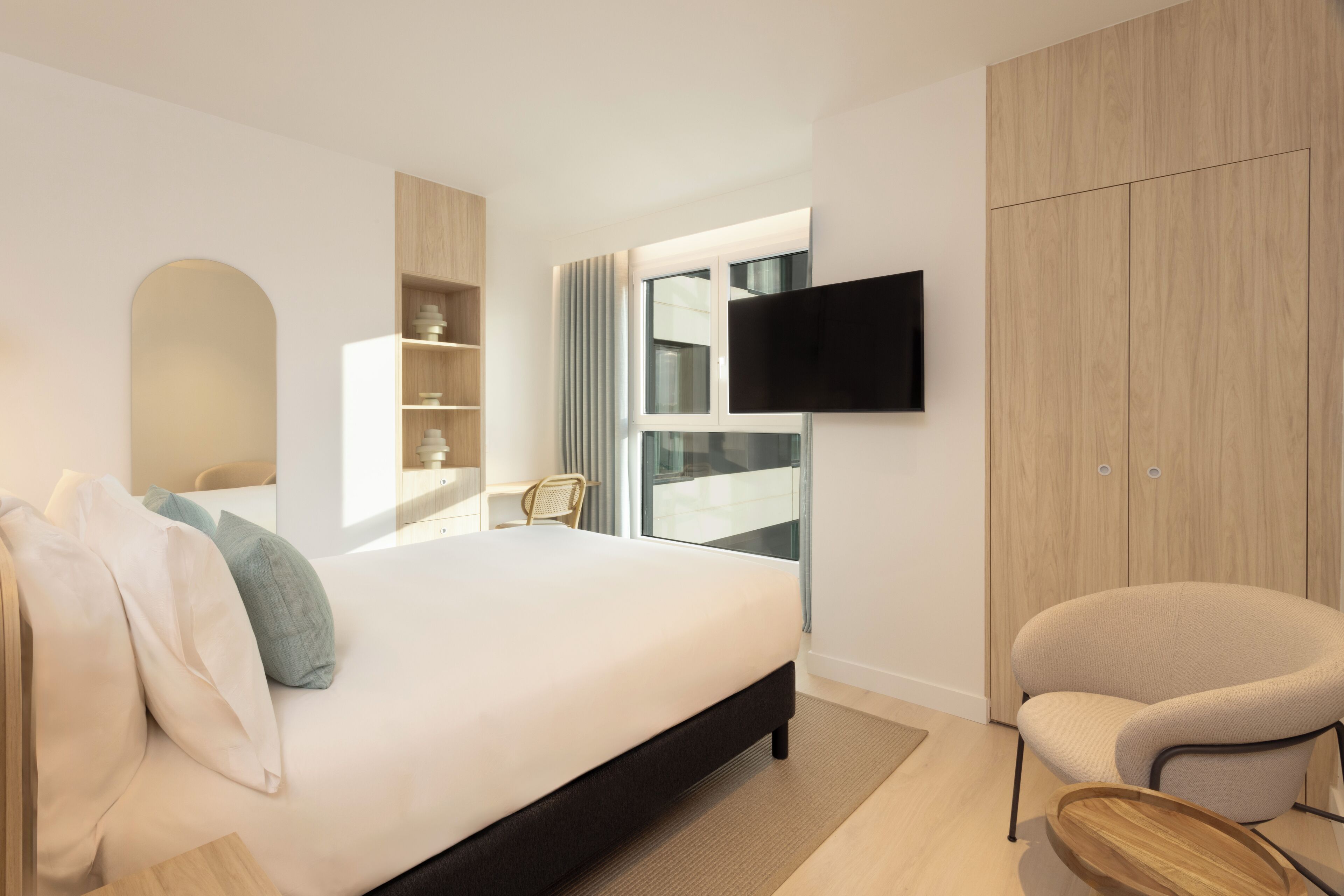 Ett modernt hotellrum med en stor säng, en platt-TV som är monterad på väggen, en garderob i trä och en sittgrupp med en stol.