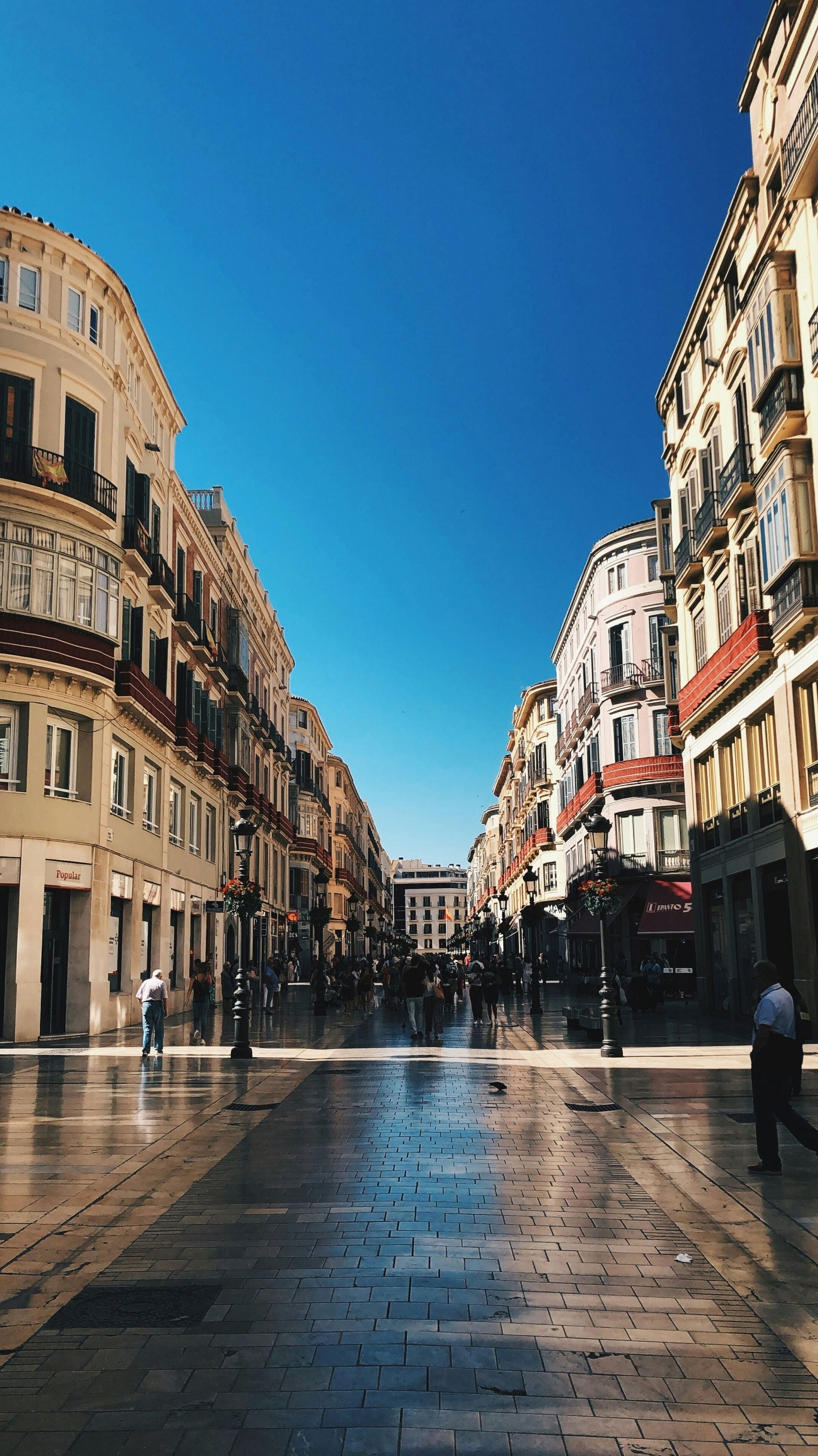 A wide, open plaza with historic buildings on either side, featuring a mix of architectural styles and a clear blue sky above.