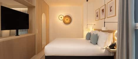 Una habitación de hotel moderna con una cama grande, un televisor de pantalla plana, una mesita de noche con lámpara y un aplique de pared.