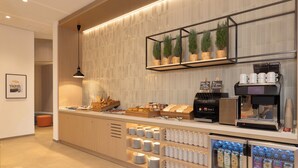 Una barra de desayuno moderna con una máquina de café, dispensadores de leche y una variedad de alimentos para el desayuno.