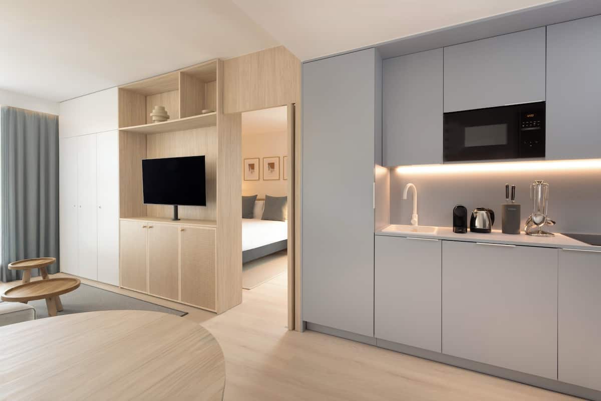 A modern hotel room with a TV, kitchenette, and a bed with a view.