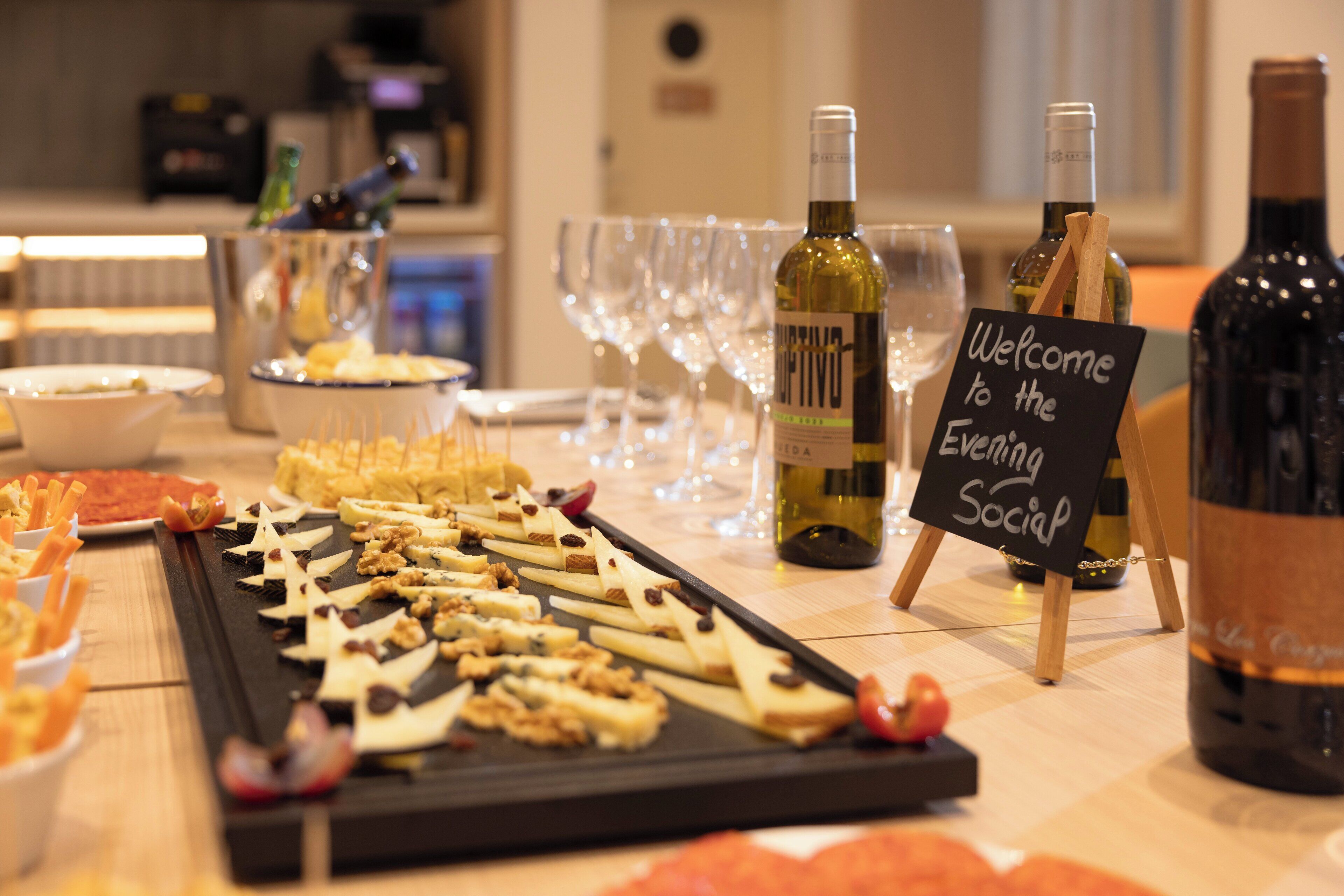 Una mesa de buffet con diversos alimentos y botellas de vino, un cartel que dice "Welcome to the Evening Social".