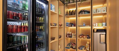 A well-organized beverage refrigerator stocked with various drinks, adjacent to a neatly arranged shelf with snacks and condiments.