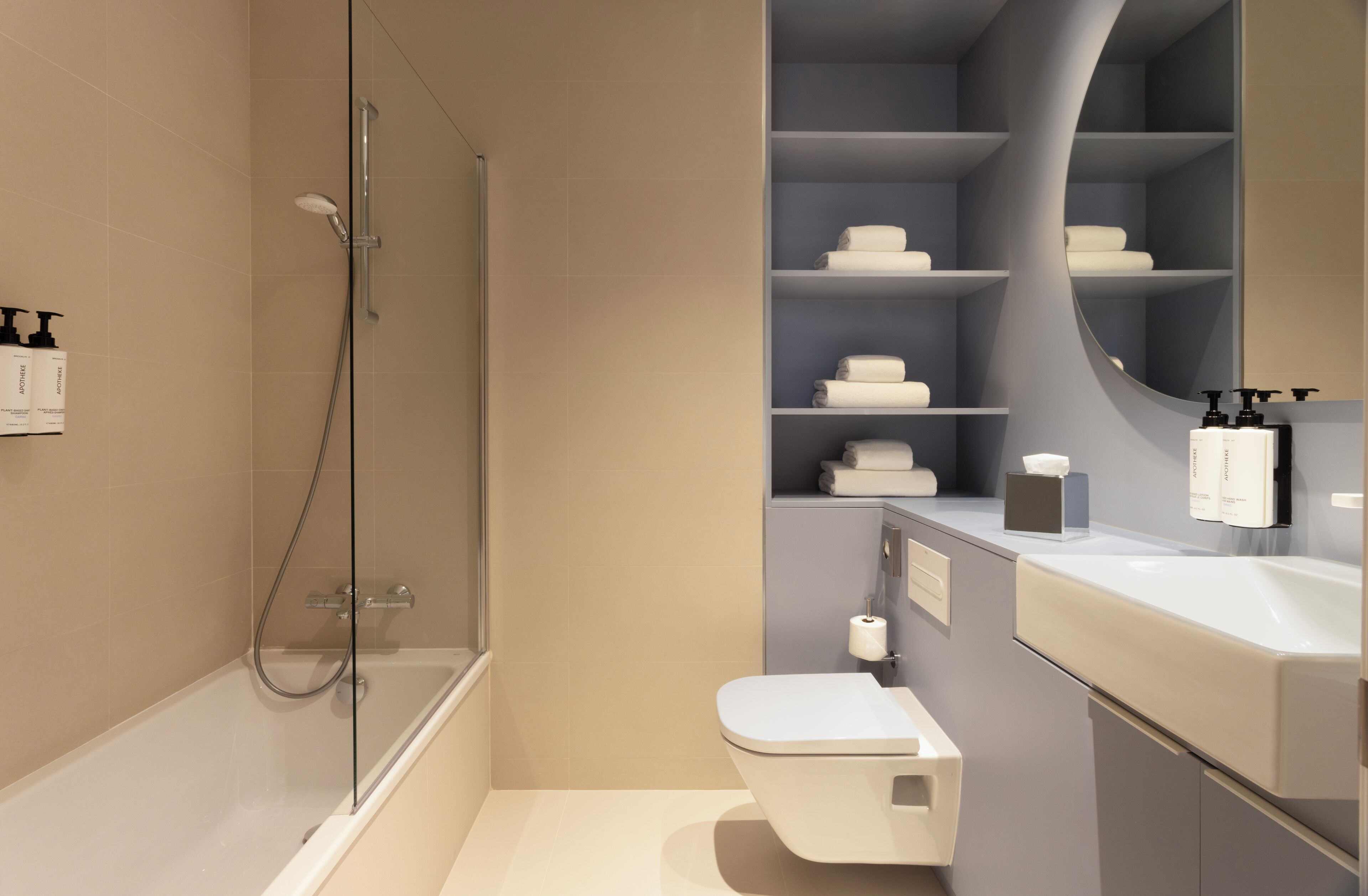 Un baño moderno con ducha envuelta en vidrio, inodoro y tocador con estantes para artículos de tocador.