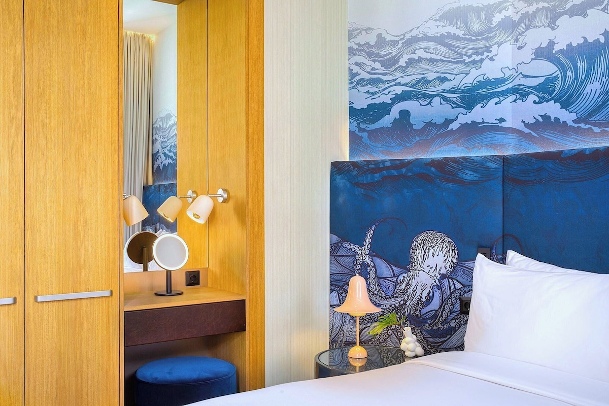 Een hotelkamer met een houten garderobe, een bed met wit beddengoed, een blauwe hoofdbord en een groot schilderij van een golf.