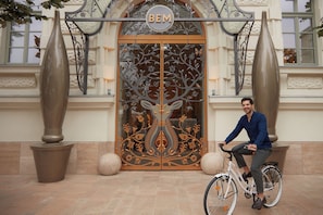 A man sitting on a bicycle in front of a building with a decorative entrance and the letters "BEM" above it. - Kimpton BEM Budapest by IHG (Budapest)