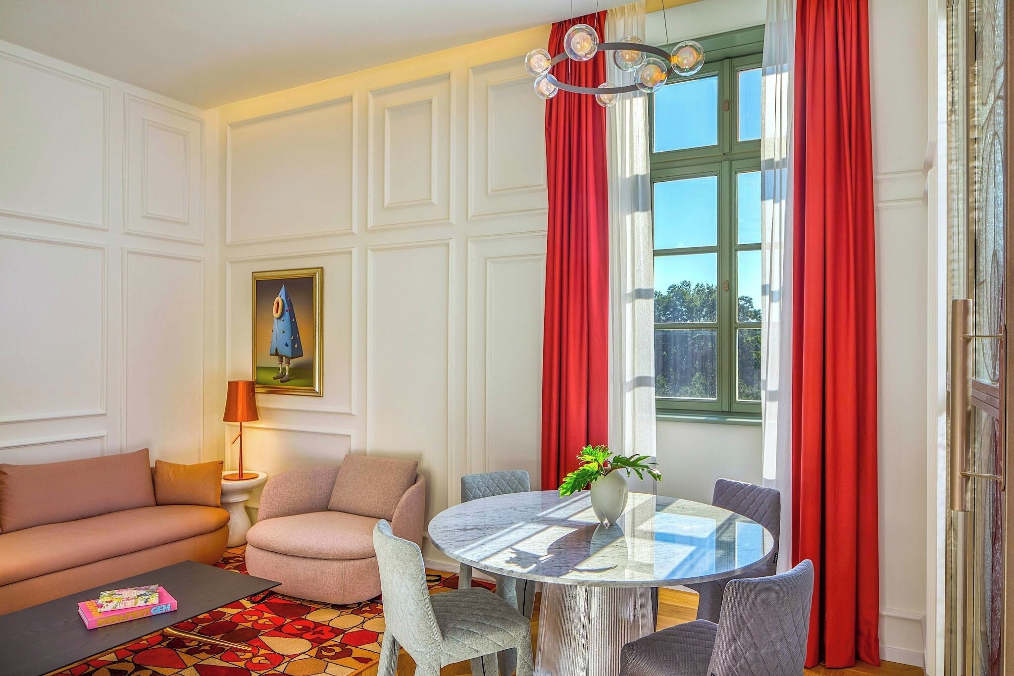 A living room with a sofa, armchair, round table, and a painting on the wall.