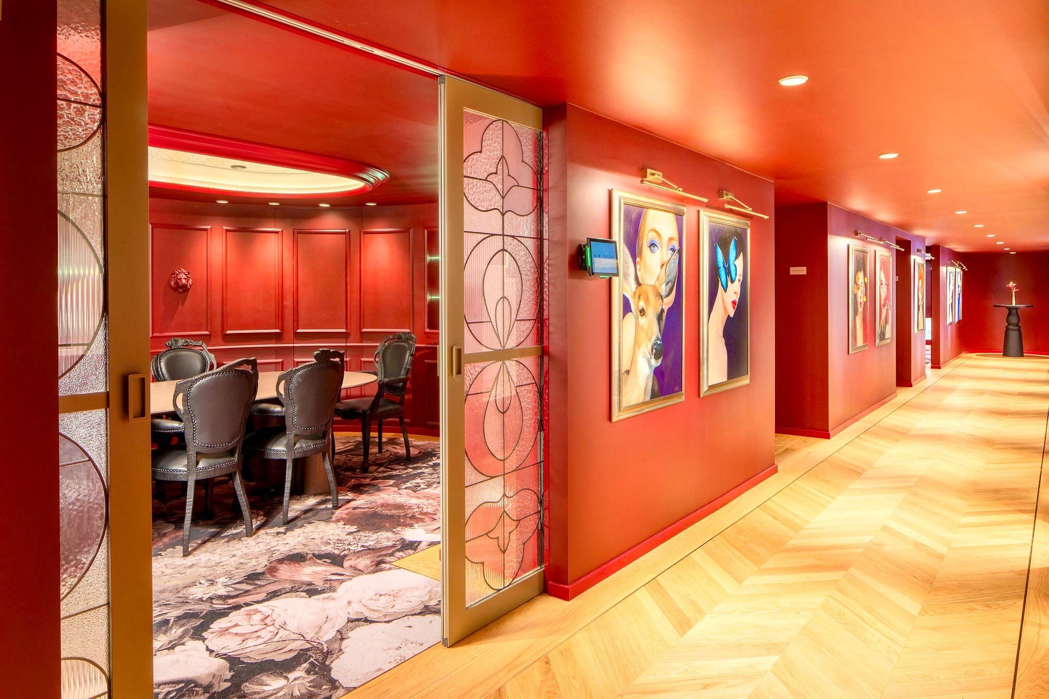 Een hotelgang met een rode muur, een eetgedeelte met stoelen en een tafel, en kunstwerken aan de wanden.