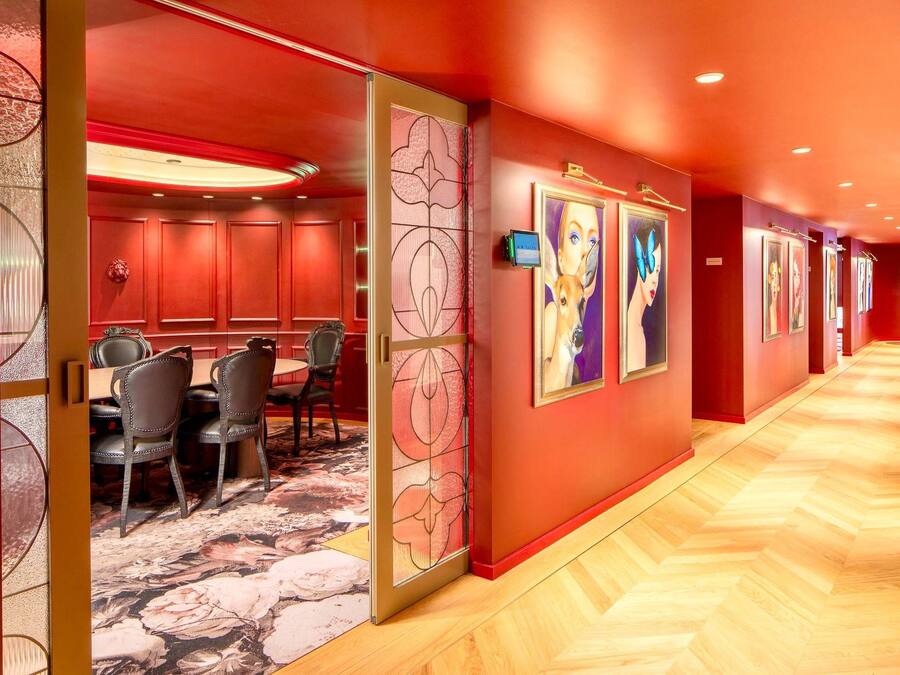 Een hotelgang met een rode muur, een eetgedeelte met stoelen en een tafel, en kunstwerken aan de wanden.