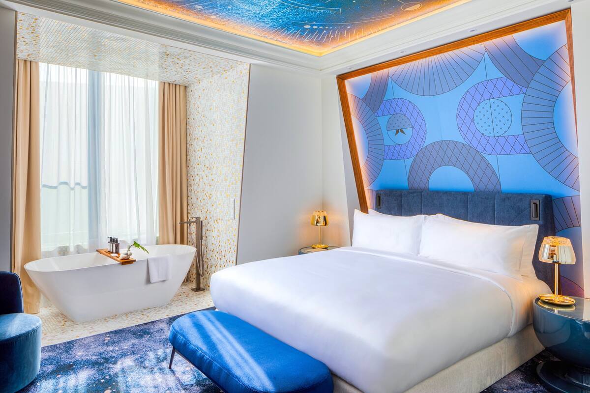 Ett modernt hotellrum med en stor säng, ett badkar och ett tak med ett geometriskt mönster.
