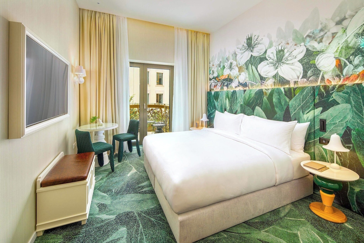 Een hotelkamer met een bed, een bureau, een stoel, een klein tafeltje en een wand met een bloemenmural.