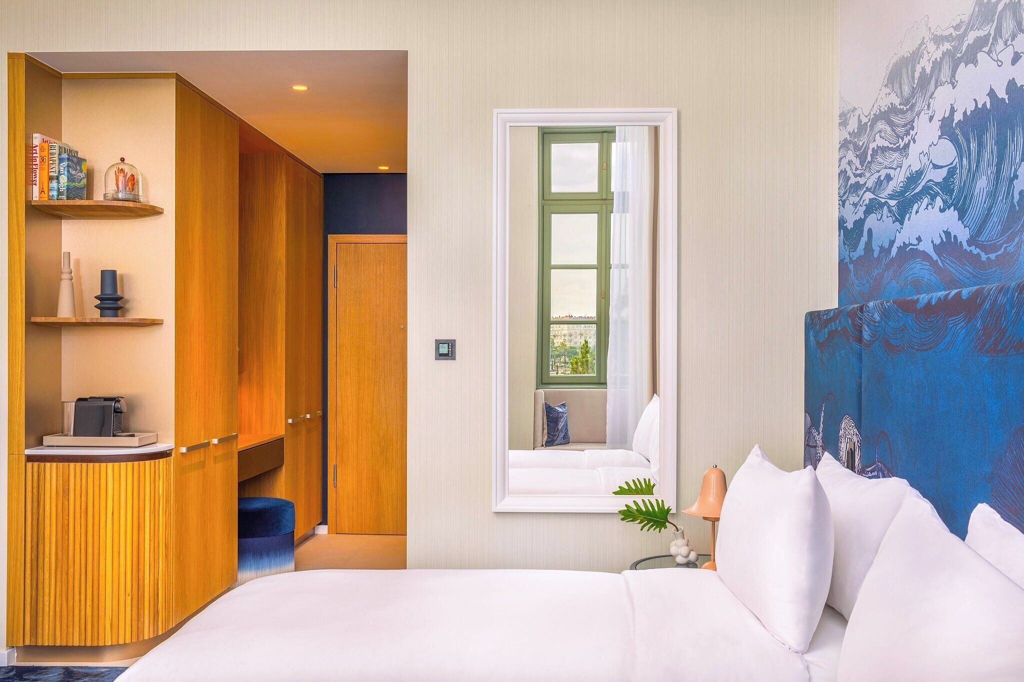Une chambre d’hôtel avec un lit, une fenêtre donnant sur un paysage agréable, une bibliothèque et un tableau accroché au mur.