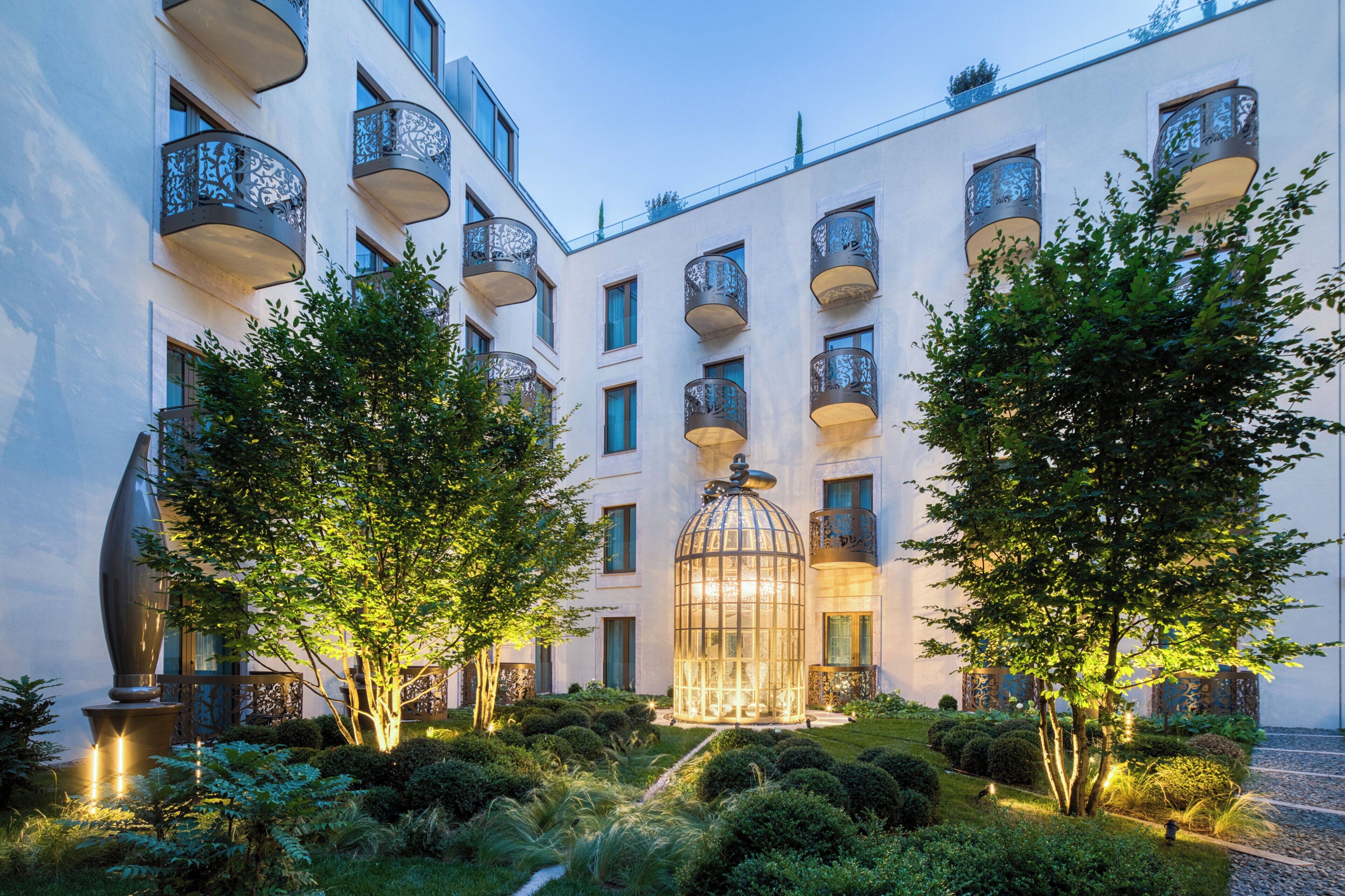 A courtyard with a glass-enclosed structure, surrounded by trees and a well-maintained garden.