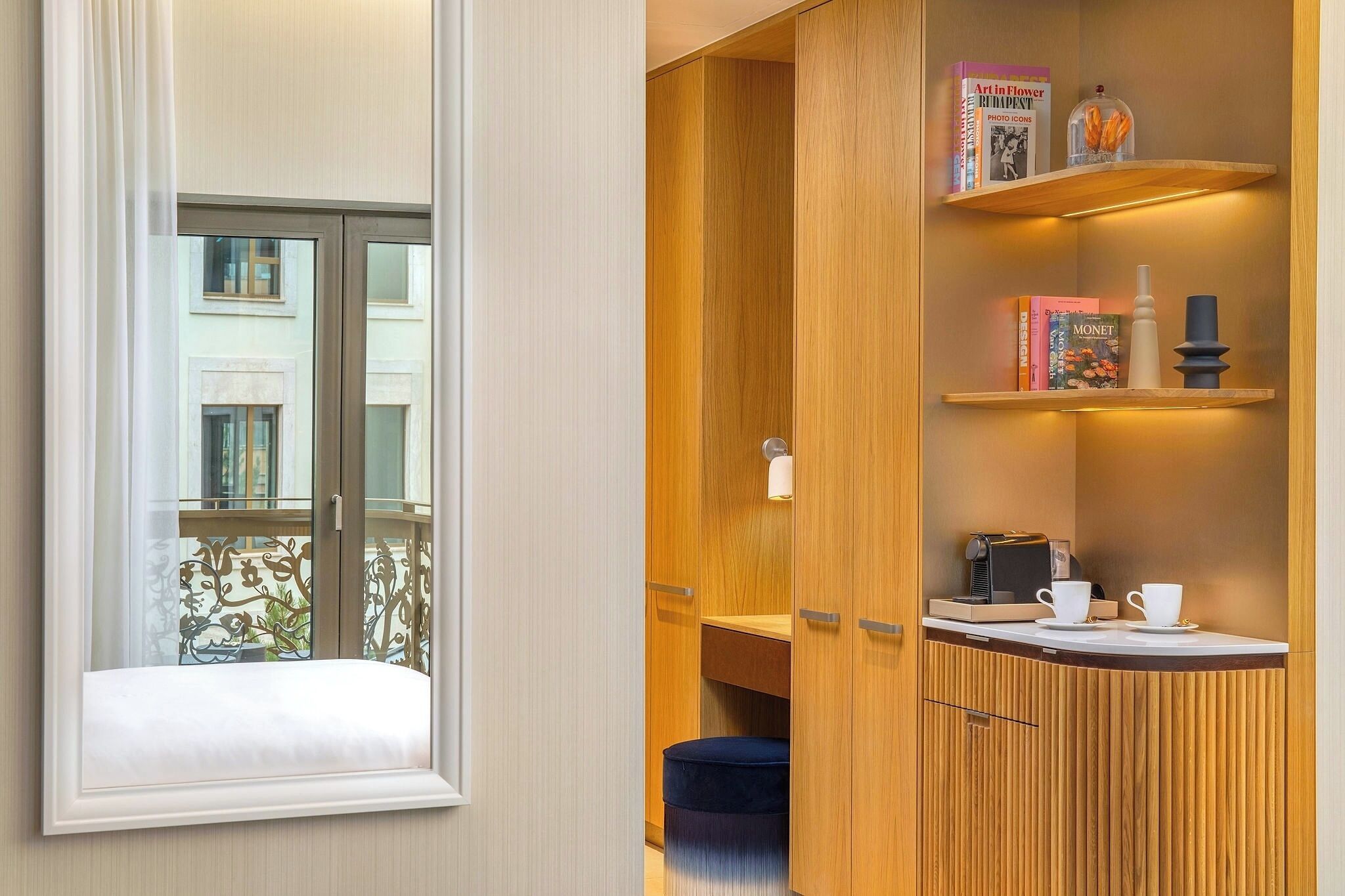 A room with a window, a wooden cabinet with shelves, and a small table with cups and a coffee maker.
