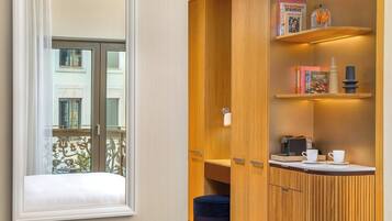 A room with a window, a wooden cabinet with shelves, and a small table with cups and a coffee maker.