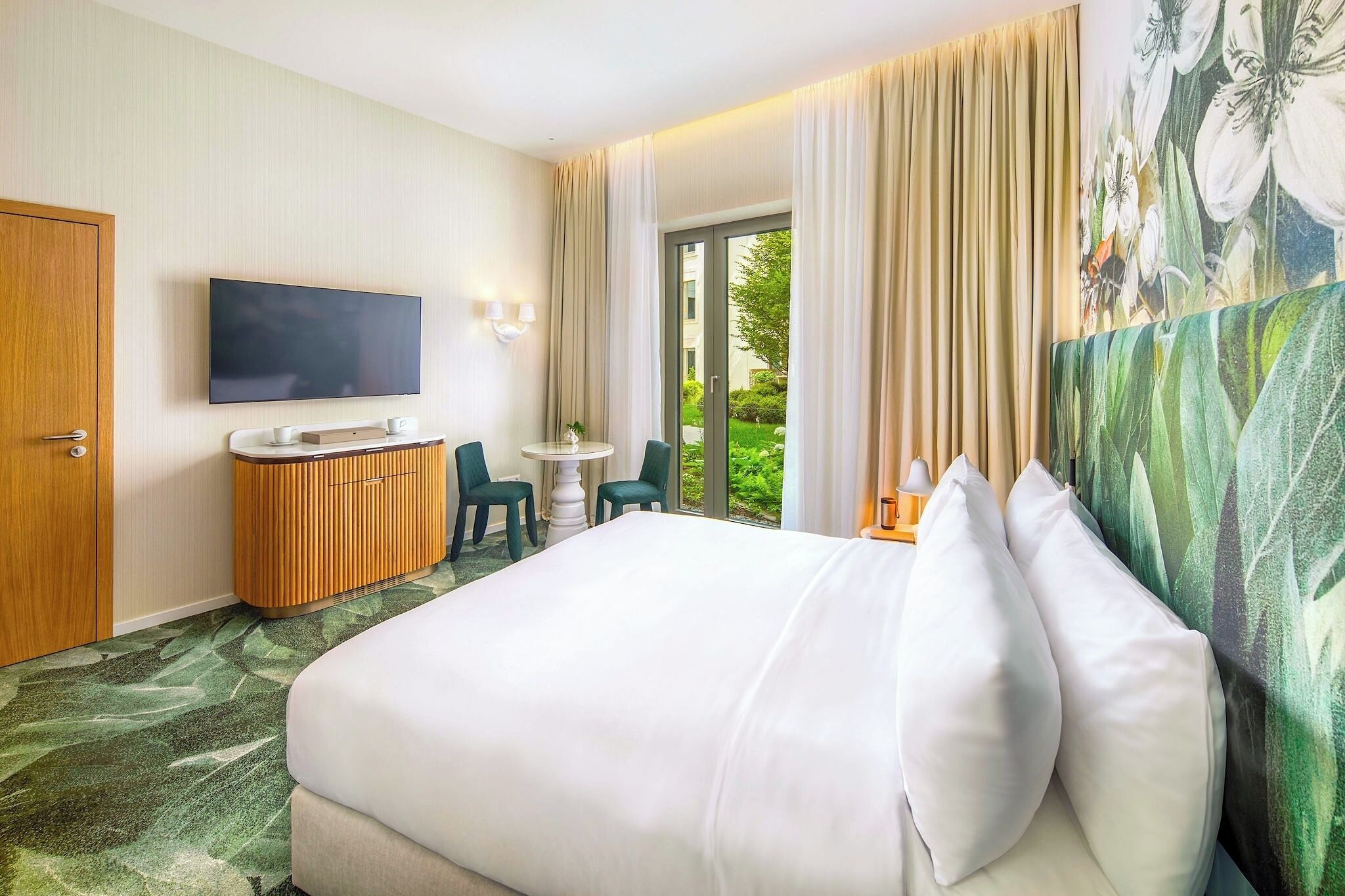 Ein Hotelzimmer mit Bett, Schreibtisch, Fernseher und Blick auf Grünflächen.