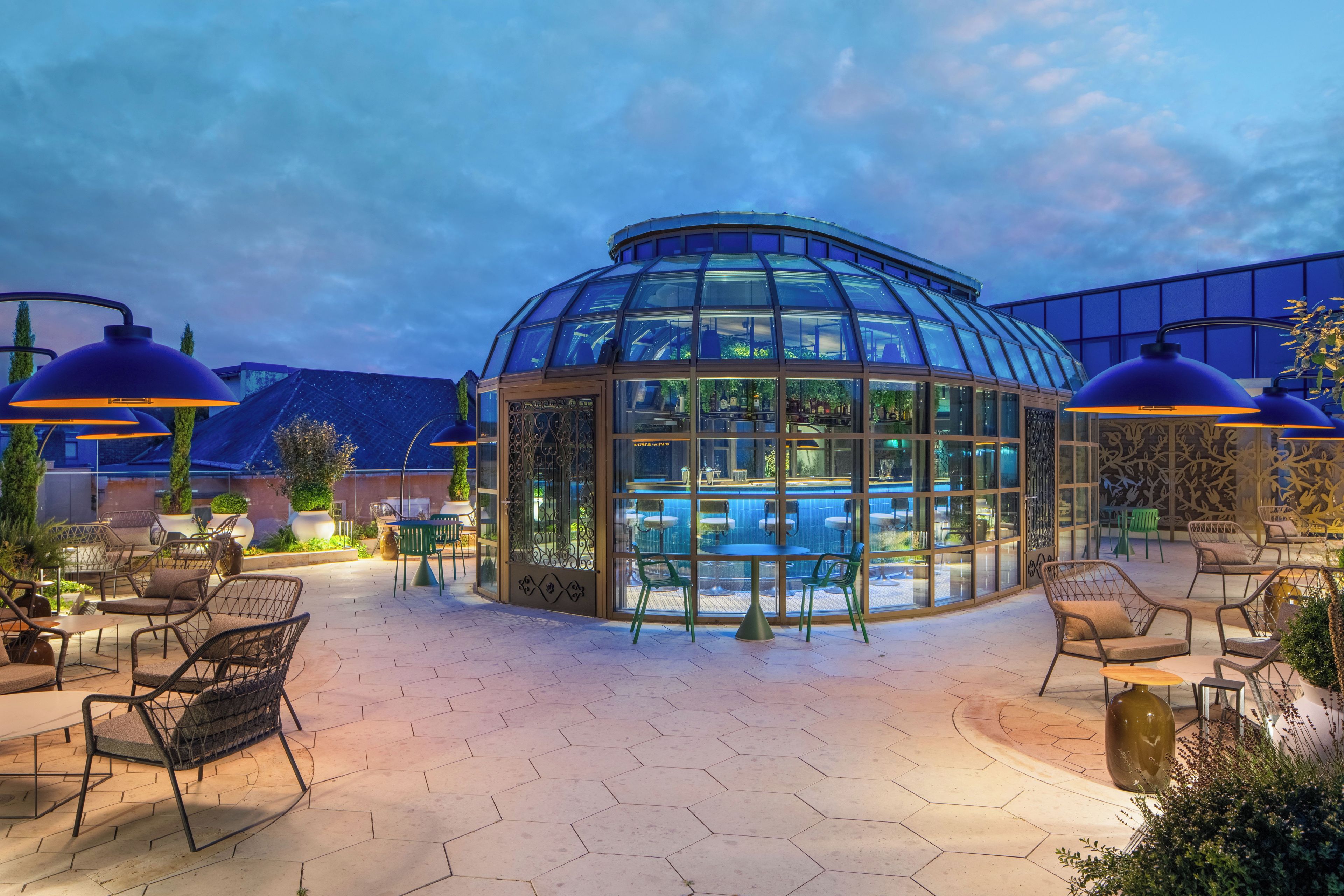 Un espace piscine entièrement vitré, doté de carreaux hexagonaux, d’un coin salon extérieur et d’un éclairage suspendu.