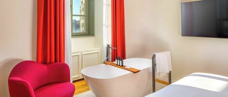 A modern bathroom with a freestanding bathtub, a red chair, and a large window with curtains.