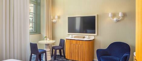 Habitación de hotel con cama, escritorio con televisor de pantalla plana, dos sillones, una mesita y una planta decorativa.