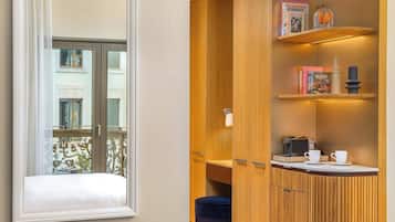 A compact room with a wooden cabinet, a small table with cups, and a window overlooking a balcony.