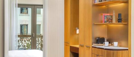 Una habitación compacta con un armario de madera, una mesita con tazas y ventana con vistas a un balcón.