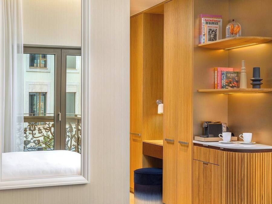 A compact room with a wooden cabinet, a small table with cups, and a window overlooking a balcony.