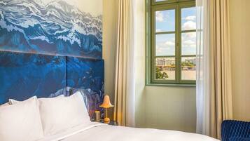 Une chambre d’hôtel avec un lit, une table de chevet avec une lampe, une fenêtre avec des rideaux et une fresque murale.