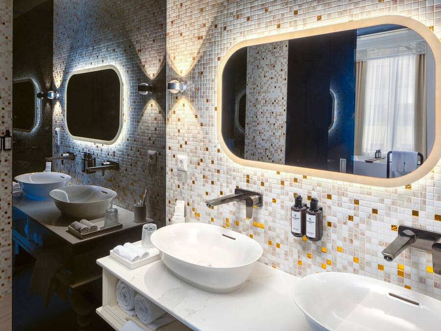 Une salle de bain moderne avec deux lavabos, un grand miroir et un pare-feu en carreaux.