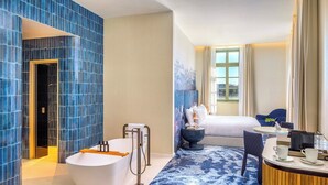 Un baño de hotel moderno con una bañera grande, una ducha y una zona de estar con mesa y sillas.